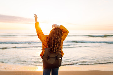 A beautiful woman with a backpack strolls along the shore at dawn. The traveler enjoys the seascape...