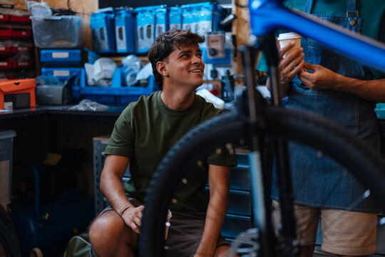 Bicycle mechanic talking with customer holding coffee in repair shop