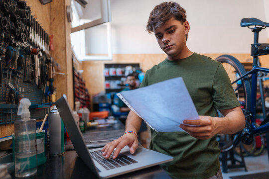 Bicycle mechanic using laptop and reading document in workshop