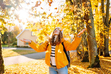 A sweet woman is having fun with fallen leaves in an autumn park. A beautiful woman tosses autumn leaves into the air at sunset. Concept of seasonality, fun, and relaxation.