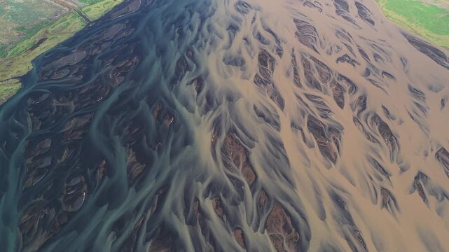 Aerial view of a braided river with contrasting light and dark waters flowing through a landscape, creating a stunning natural spectacle, Sk&uacute;mssta&eth;ir, Iceland.
