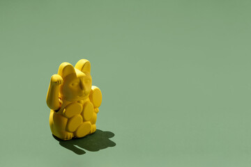 Yellow maneki-neko figurine on green background with copy space