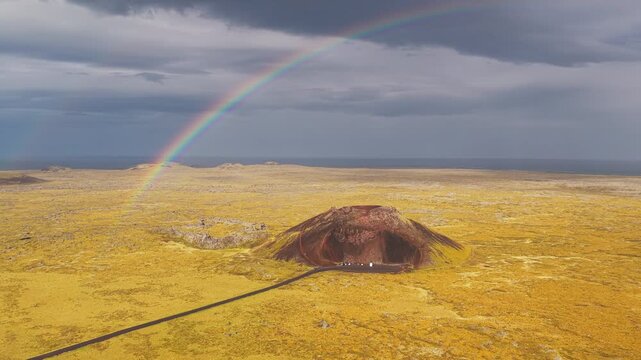 Aerial view of the Saxh&oacute;ll Crater under a rainbow, where the dark volcano contrasts with the surrounding golden plains, Hellissandur, Sn&aelig;fellsb&aelig;r, Iceland.