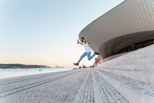 Man jumping on steps at MAAT Lisbon waterfront at sunset