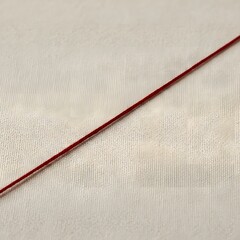 Close Up View Of A Thin Red Thread Stretching Across A Textured Fabric Surface
