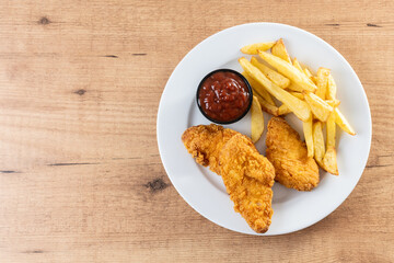 Crispy fried chicken tenders with french fries on wooden table. Top view. Copy space