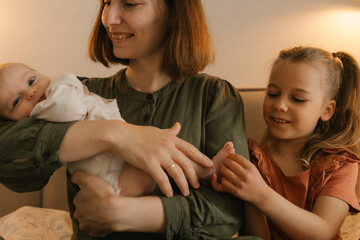 Mother with young baby and girl bonding indoors in affectionate moment