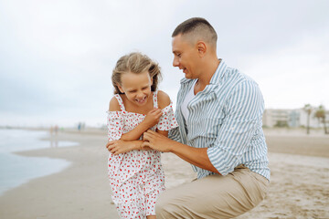 A father and his little daughter stroll along the seashore, holding hands. A happy man and his child are having fun, enjoying time together outdoors. A concept of childhood, relaxation.