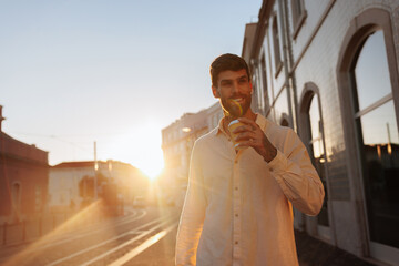 Handsome young manager drinking takeaway coffee at sunset in the city