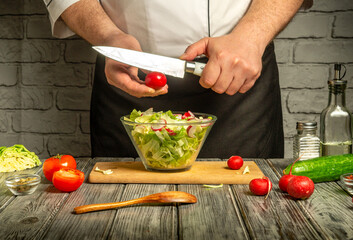 A chef with a knife skillfully chops cherry tomatoes while preparing a vibrant salad in a cozy kitchen. Fresh greens and vegetables are arranged nearby