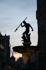 Obraz premium Neptune's Fountain at night, historic fountain in Gdansk, Poland. One of the most known landmarks of the city. View with city buildings in the background.