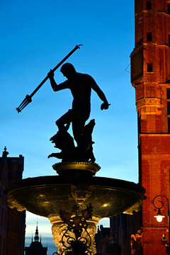 Neptune's Fountain at night, historic fountain in Gdansk, Poland. One of the most known landmarks of the city. View with city buildings in the background.