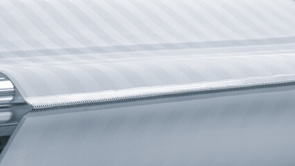 Roll of white fabric is being fed through a machine. The machine is made of metal and has a silver...