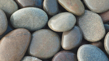 Pebbles round stones on the sea beach are illuminated by the morning sun and have warm sunny shades as a textured SPA background for page design template