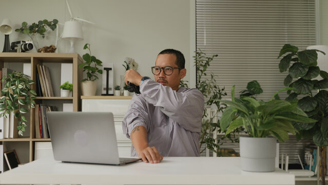 Asian man video calling friends while using electric massager at home.