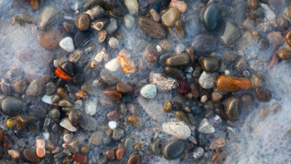 Pebbles, round, smooth, wet, colorful, on the sea beach, with water and sea foam with bubbles...