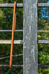 A rusty metal bar is suspended from a deteriorating structure, with vibrant green trees providing a natural backdrop under clear blue skies.