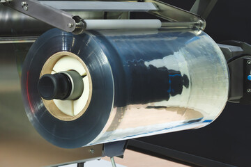 A machine with a roll of polyethylene plastic wrapping film on it. The machine is in a factory....
