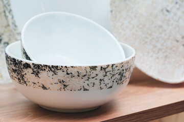 White bowl with a gold rim sits on a wooden shelf. The bowl is the center of attention, and the surrounding area is minimalistic.