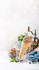 Chocolate ice cream cone with a waffle texture, placed in a glass dish alongside fresh mint leaves and a cozy blue cloth, phone background with copy space