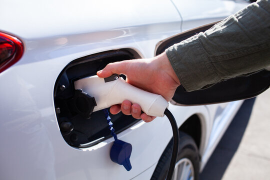 Man plugging in Hybrid vehicle electric charging plug into port on sunlit day