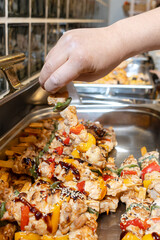 Hand takes grilled chicken and vegetable skewer with sauce and sesame seeds