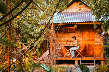 Close up young caucasian hipster woman sit use computer freelance do freelancing work, write travel blog or browse internet search, work online while traveling in southeast asia tropical islands