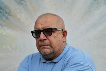 Caucasian mature man with beard wearing sunglasses and blue polo shirt with serious expression.