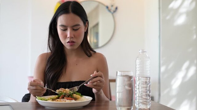 Beautiful young woman eating famous Thai holy basil Pad Krapow Asian food in restaurant during day