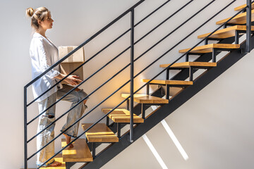 Young woman with boxes walking up stairs at home. Moving day.