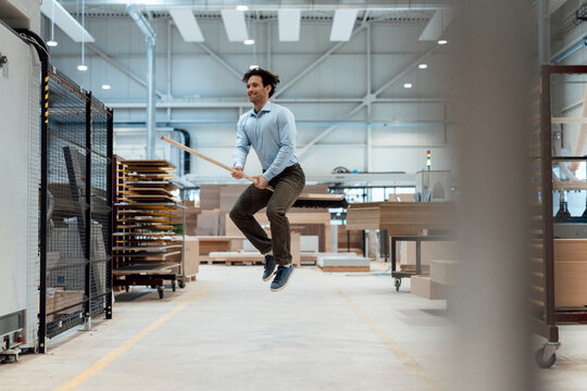 Happy businessman jumping with broom in industry