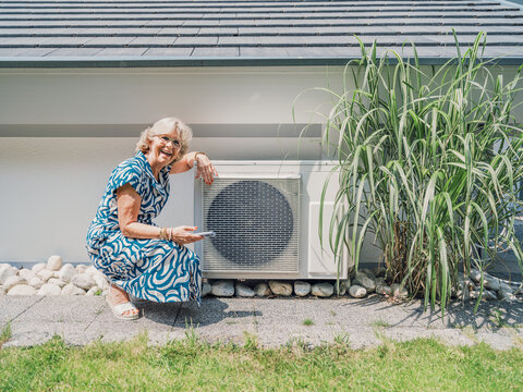 Smiling woman adjusting heat pump with smartphone in home garden