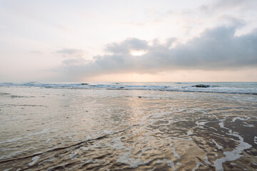 Seascape. Soft waves roll onto a sandy beach as the sun sets in the background. Peaceful landscape. Wildlife concept.