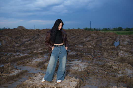 Young woman in casual outfit standing on muddy construction field at evening
