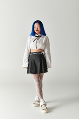 Trendy young woman with blue hair showcases unique fashion in a grey studio setting