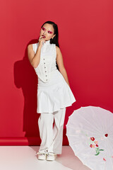 Young woman displays vibrant fashion and striking eye makeup in a red studio