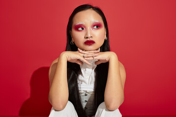 Beautiful young woman showcases vibrant eye makeup in a trendy red studio setting