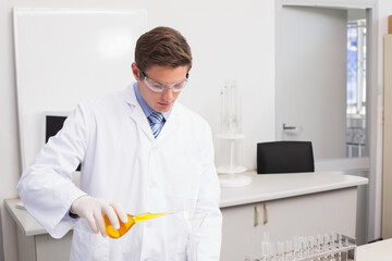 Erlenmeyer flask pouring bright yellow solution through glass funnel into beaker on white lab bench