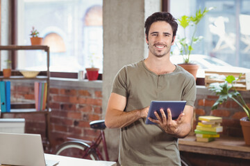 Man standing in modern loft office holding tablet near desk with laptop, bicycle and potted plants