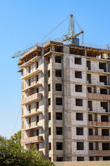 Skyscraper in construction phase with crane. High residential tower with crane under construction against blue sky. Symbol of modern city growth and real estate projects.