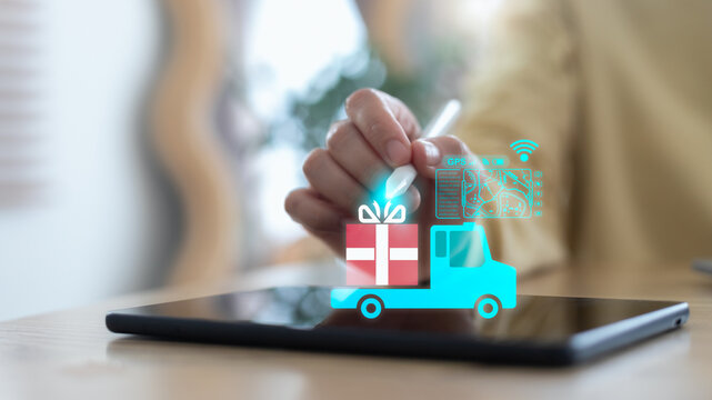 Close-up of a hand using a digital tablet with a hologram of a delivery truck, gift box, GPS tracking, and smart logistics technology concept for e-commerce shipping and online business.