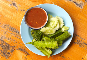 Traditional Thai food side dish, fresh and steamed vegetables and spicy salty sauce from shrimp paste and herbs - called Nam Prick in Thai language. Top view food image on wooden table.