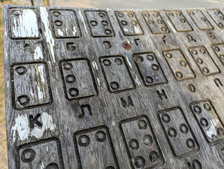 An old crumbling sign with the Braille alphabet. A decrepit plywood with paint drips. A vintage wood with a cracked surface. The Braille alphabets from A to Z in alphabetical order.
