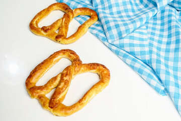 Closeup view of a pretzel loaf with a blue checkered tablecloth or napkin in a white table background. Concept of Oktoberfest. Bavarian German culture festival decoration symbol