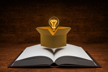 A book on a table with a box containing a light bulb represents a box of ideas, learning, education, searching, and inspiration.