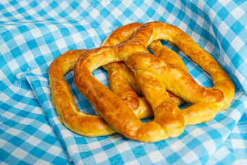 Closeup view of a pretzel loaf with a blue checkered tablecloth or napkin background. Concept of Oktoberfest. Bavarian German culture festival decoration symbol