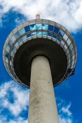 Skyward view of a modern observation tower reaching into a vibrant blue sky adorned with fluffy white clouds