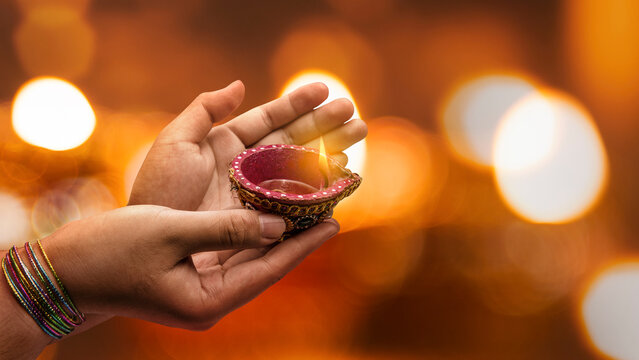 Woman hand holding a lit clay diya lamp with a blurred bokeh light background. Celebration of Diwali or Deepavali Hindu Festival