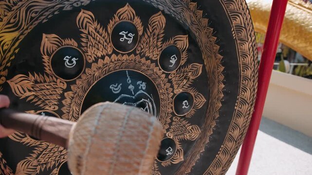 Ornate golden temple gong striking by buddhist monk during traditional spiritual ceremony, revealing intricate details and meditative resonance, Thailand.