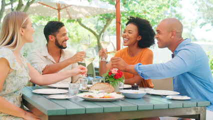 Group Of Friends Enjoying Outdoor Meal And Wine On Visit To Vineyard Restaurant